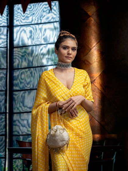 A model in a bright yellow polka-dot saree, shot indoors but with a large window providing natural light. This image blends indoor comfort with an outdoor feel, showcasing the versatility of the attire.