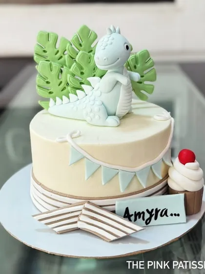 A cute dinosaur-themed cake with a friendly fondant dinosaur on top. The design is complemented by edible monstera leaves and a matching mini cupcake.