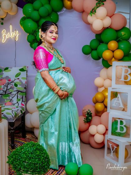 Another beautiful full-length shot of the mother-to-be at her baby shower, showcasing her stunning saree and the festive decorations.