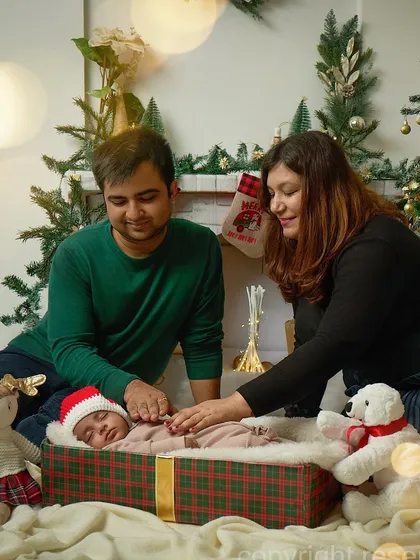 Parents gently watch over their sleeping newborn, who is beautifully presented in a gift-wrapped box under the Christmas tree. This is the most precious gift of all.