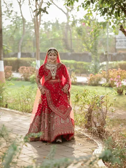 The bride taking a stroll in the garden, looking absolutely radiant in her red lehenga. A beautiful full-length bridal portrait.