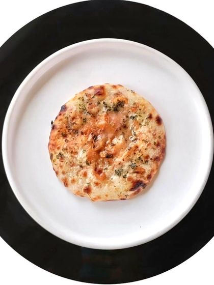 A single, perfectly round kulcha, topped with herbs and baked to perfection. It represents the simple elegance that underlies even our most inventive creations.