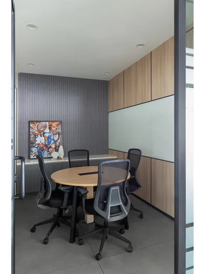 A smaller meeting room designed for team huddles. It features a round table to encourage inclusive discussion, fluted wall paneling for texture, and a vibrant piece of art to spark creativity.