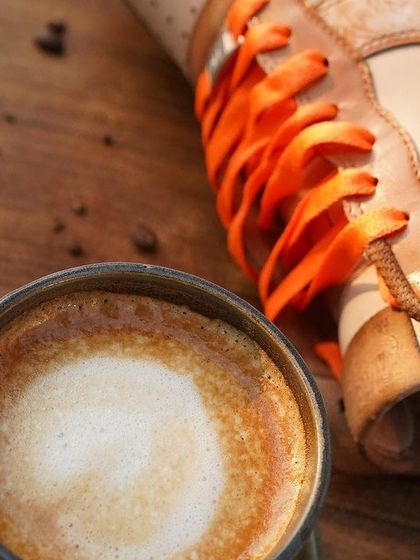 A close-up showing the rich texture of the coffee-dyed leather next to a cup of coffee. The Toile de Jouy print is subtly visible, showcasing the intricate detail of the artwork.