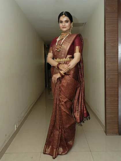 A full-length shot that captures the grandeur of the South Indian bridal look. The makeup is balanced to complement the magnificent saree and heavy jewellery, creating a regal appearance.