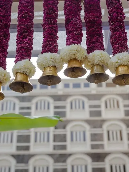 A detail of the entrance arch, showing the intricate weaving of purple flowers and the hanging brass bells against the iconic facade of the Taj Mahal Palace hotel.