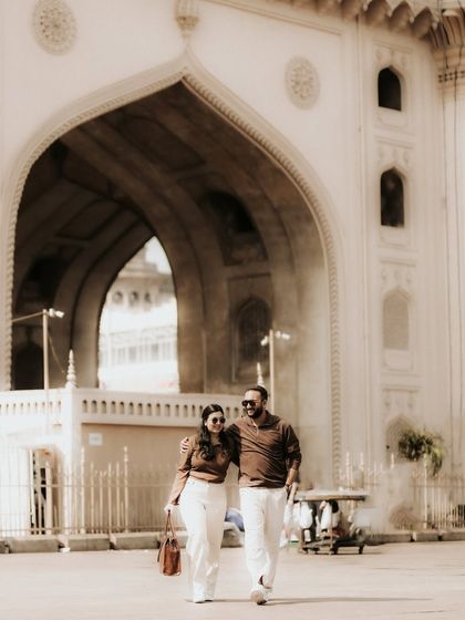 A candid shot of the couple walking through a historic archway. This photo captures a relaxed moment of their pre-wedding shoot, blending modern style with old-world charm.