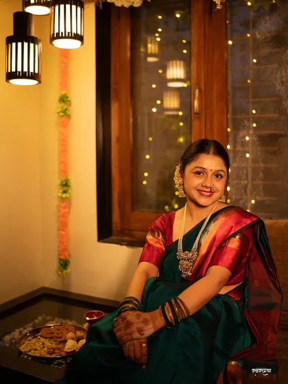 A relaxed and happy portrait from a Diwali shoot. The model is seated comfortably at home, surrounded by festive decor, capturing a genuine moment of peace and contentment.