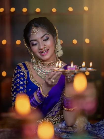 Holding a diya, the model's face is illuminated, showing the beautiful glow of the highlighter and the smooth finish of the makeup.