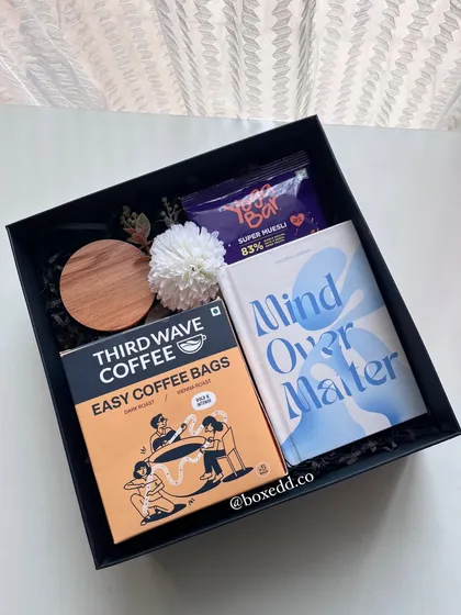 A wellness-themed gift box curated for International Yoga Day, containing easy-pour coffee, a healthy snack bar, and a journal.