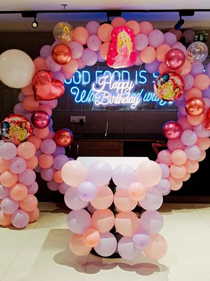 This Barbie-themed party setup features a balloon arch in shades of pink and peach. It's a simple yet elegant design perfect for a restaurant or home celebration.