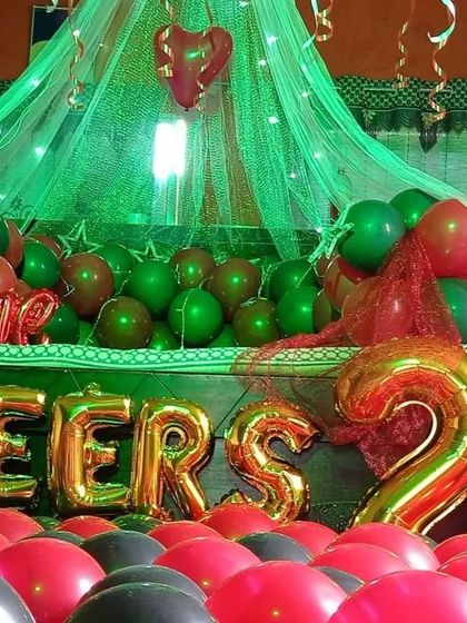 This decoration shows how lighting can change the mood. Here, a green light is used with a canopy and balloons to create a unique and different kind of romantic ambiance for a milestone celebration.