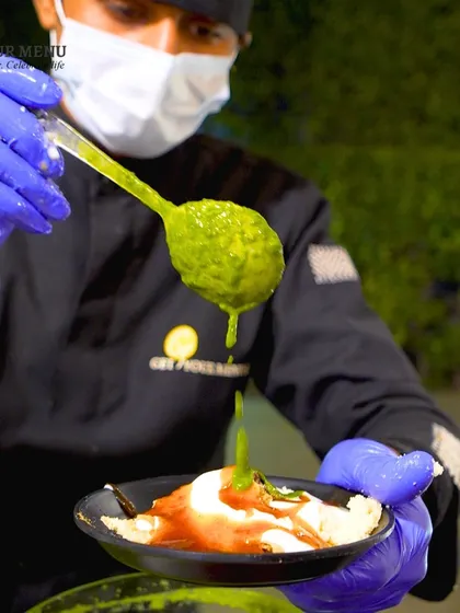 The final touch. A chef adds a spoonful of vibrant green mint chutney to a plate of Dahi Bhalla, ensuring the perfect balance of flavours.