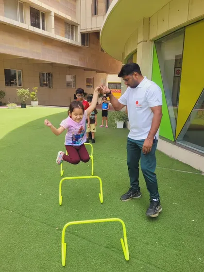 With the help of an instructor, a young girl joyfully leaps over hurdles. Our PT drills are designed to build confidence and motor skills in a supportive and encouraging environment.