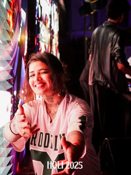 A playful moment, pointing at the camera and sharing a smile during a fun Holi performance.