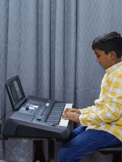 A young student in a yellow checkered shirt plays the keyboard at an open mic.
