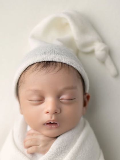 A close-up of a peacefully sleeping newborn, wrapped in white. A timeless and classic portrait.