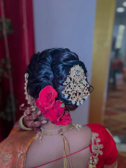 This is a classic bridal khopa, elevated with deep red roses and an ornate jeweled accessory. I build the bun to be full and balanced, ensuring it looks perfect from every angle and securely holds the weight of the flowers and jewelry. This style is a statement of pure bridal opulence.