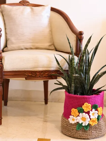 A quiet corner featuring one of my two-toned crochet baskets used as a beautiful planter cover. The bright pink top half is decorated with delicate white and yellow crochet flowers.