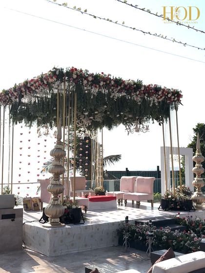 A side view of the modern seaside mandap, showcasing its clean golden frame, lush floral canopy, and the open, airy feel perfect for a beach wedding.
