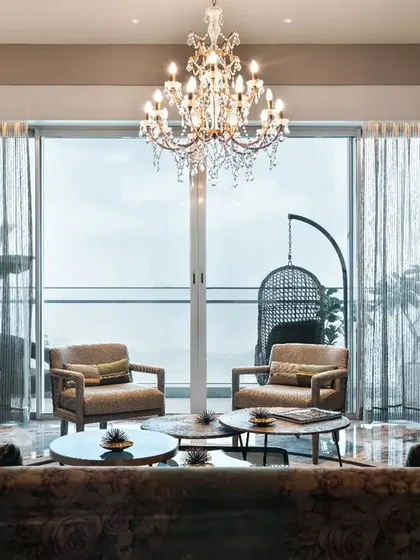 The main seating area is oriented towards the balcony to maximize the incredible city view. A grand crystal chandelier anchors the space, while the white marble window jamb creates a seamless transition to the outdoors.