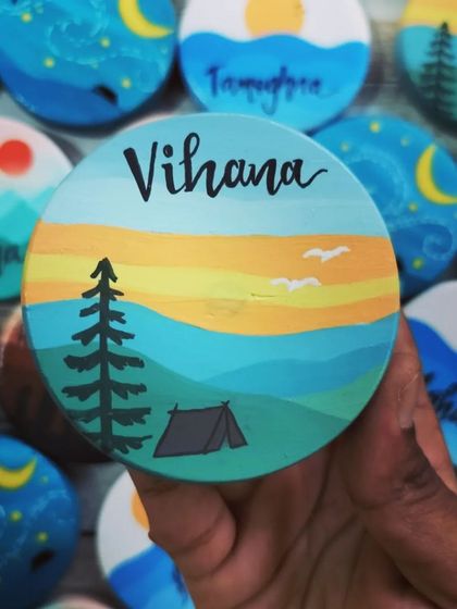 A camping scene at sunset, hand-painted on a small wooden magnet for "Vihana." These tiny pieces of art are full of detail and character.