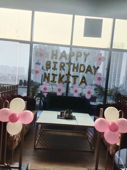 A simple birthday setup in a restaurant with pink and white flower-shaped balloon bunches and foil letters.