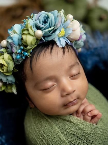 A close-up on the baby's face, showing the intricate details of the blue and green floral crown.