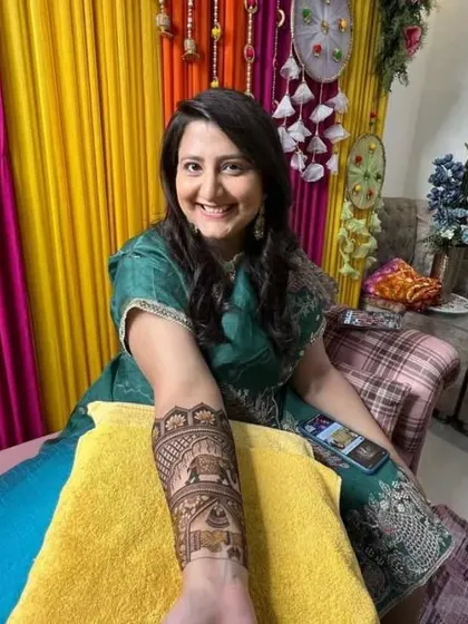 A smiling client proudly displaying her arm mehandi. The design features traditional elephant and floral motifs, perfect for her celebration.