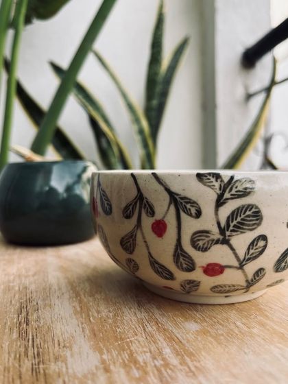 A close-up of a student's hand-painted bowl with a delicate berry and leaf design.