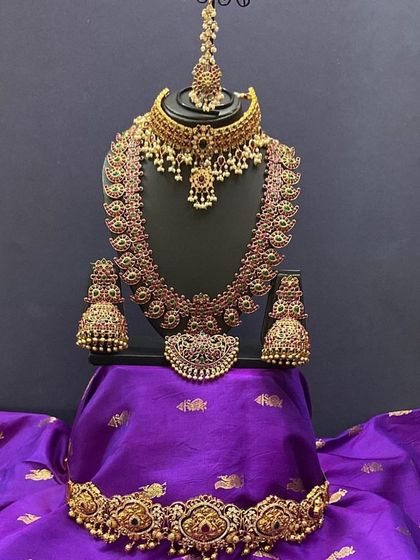 This bridal set features a unique combination of a kemp choker and a mango-motif long necklace. The matching jhumkas and vaddanam complete this beautiful rental set.