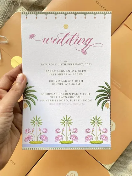 Holding the main wedding invitation from the minimal suite. The design features a delicate border of Pichhwai-inspired lotus and palm motifs, blending traditional art with a clean, modern layout.