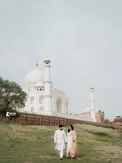 A classic walking shot with the Taj Mahal in the background. The couple's traditional white outfits complement the elegance of this iconic monument.
