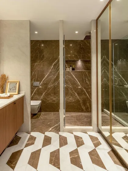This bathroom showcases a bold use of brown marble with dramatic white veining. The geometric floor tiles add another layer of pattern, while the glass shower partition keeps the space feeling open.