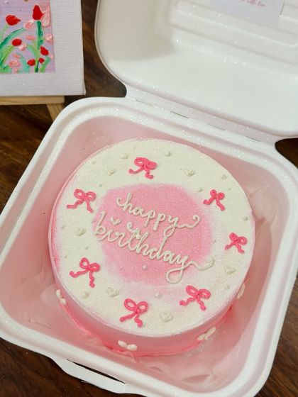 A lovely pink bento cake with an airbrushed center and delicate bow details. This coquette-style cake is perfect for a sweet and feminine celebration.