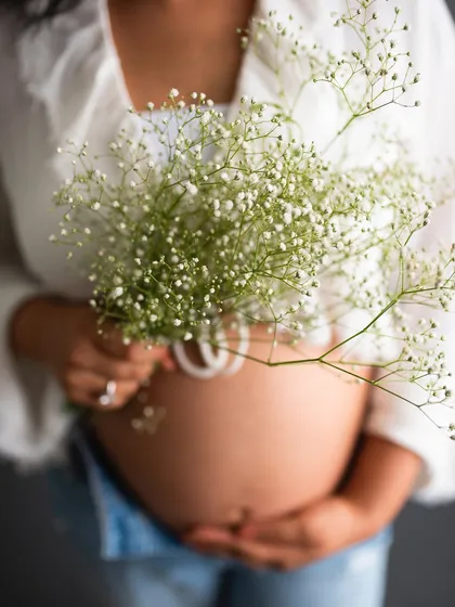 A beautiful close-up focusing on the baby bump, with the delicate baby's breath flowers adding a soft, sweet touch.