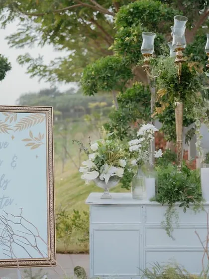 The welcome table for the 'Luxe Garden' wedding, featuring a beautiful sign and arrangements of white flowers and greenery.