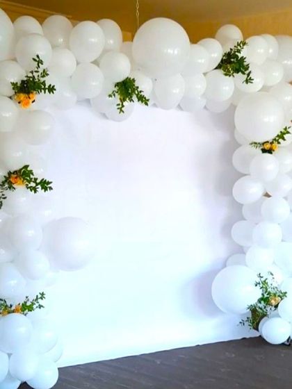 A simple and pure all-white balloon arch for a First Holy Communion. Small sprigs of greenery and flowers are tucked in for a natural touch.