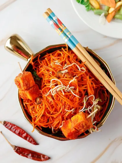 A bowl of spicy ramen noodles with paneer skewers, styled with red chillies to emphasize the heat.