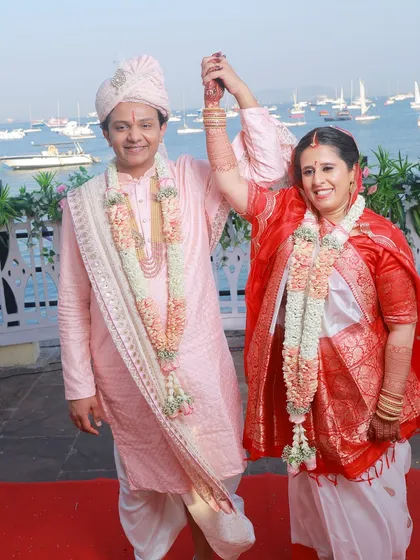 A celebratory moment captured perfectly. The bride's traditional white and red Panetar saree and the groom's coordinated outfit look stunning against the sea.