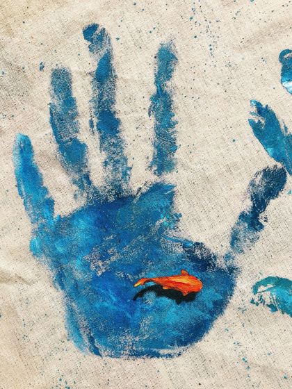 This piece, 'The Human Imprint', uses a simple handprint on a tote bag to send a message about our impact on the oceans. The small fish swimming within the print is a reminder of what's at stake.