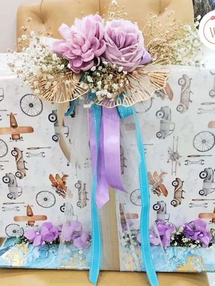 This image shows the scale of our gift wrapping services. A large gift is wrapped in quirky, fun paper and adorned with a cascade of purple and blue ribbons and flowers.