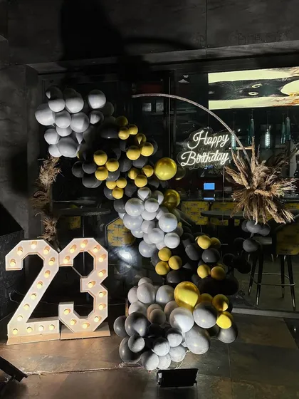 We love a good color combo! This 23rd birthday setup featured a trendy balloon arch in grey, black, and yellow, paired with marquee numbers and a neon sign for a cool, modern party vibe.