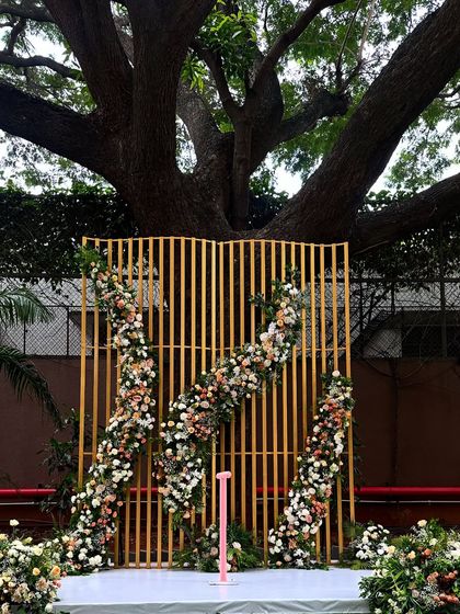 This modern Varmala backdrop was designed to complement the majestic tree it stands under. The gold-slatted screen is asymmetrically adorned with pastel peach and white roses for a contemporary look.