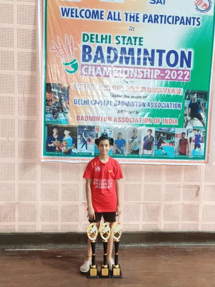 Prasidhi Gupta standing proudly with her three trophies, a triple-crown achievement at the Delhi State Badminton Championship 2022.