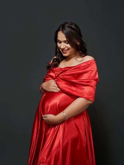 A close-up portrait of a glowing mama-to-be in our red satin gown. The off-shoulder wrap is a classic and flattering style.