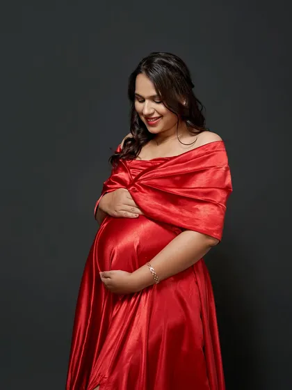 A close-up portrait of a glowing mama-to-be in our red satin gown. The off-shoulder wrap is a classic and flattering style.
