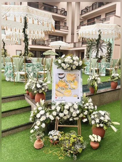 The welcome area for the "Mehndi & Mimosas" event, with a custom social-media-frame-style sign surrounded by white flowers.