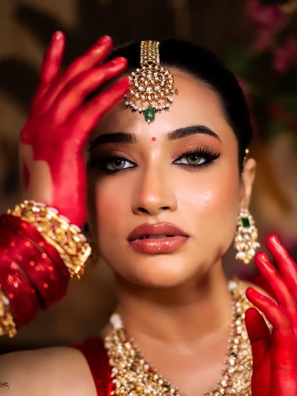 A powerful close-up of the bride with red-painted hands framing her face, her gaze intense and captivating.