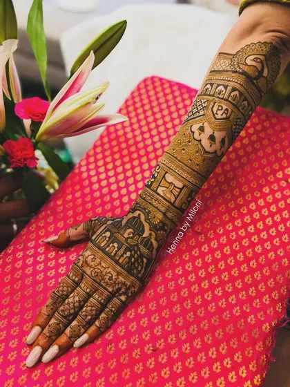 A full-arm bridal design with personalized initials 'PA'. The pattern includes peacocks, elephants, and architectural elements, covering the arm from fingers to elbow.